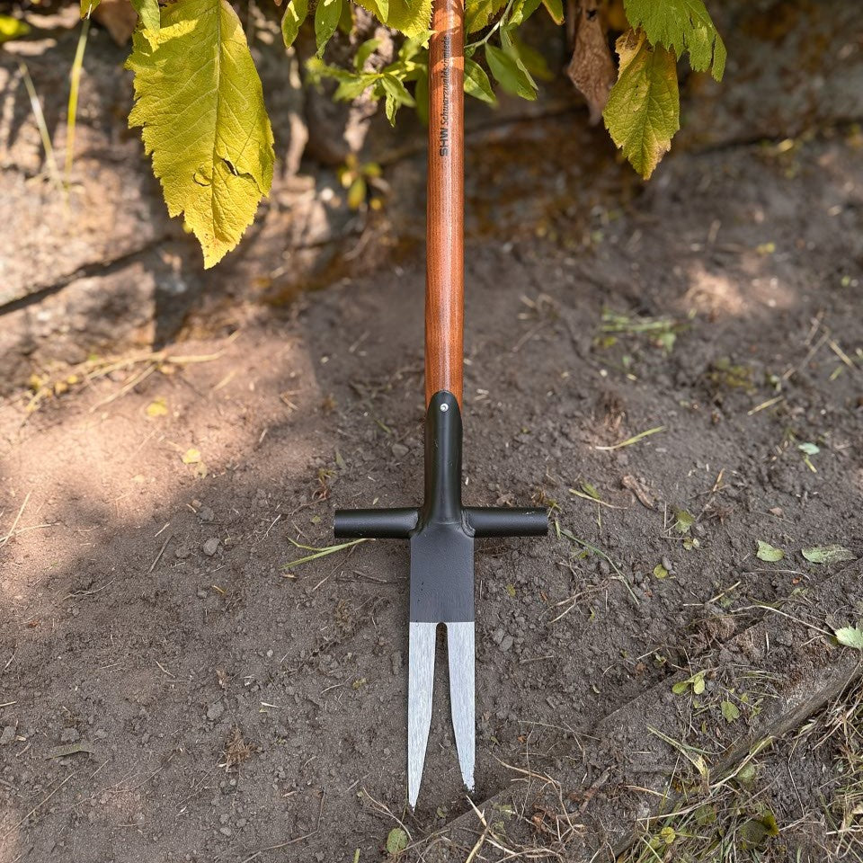 Detailaufnahme des SHW Ampferausstechers mit zwei spitzen Stahlzinken und seitlichen Tritthilfen auf Gartenboden. Werkzeug zum Ausstechen tiefwurzelnder Ampferpflanzen und anderer Wurzelunkräuter. hero