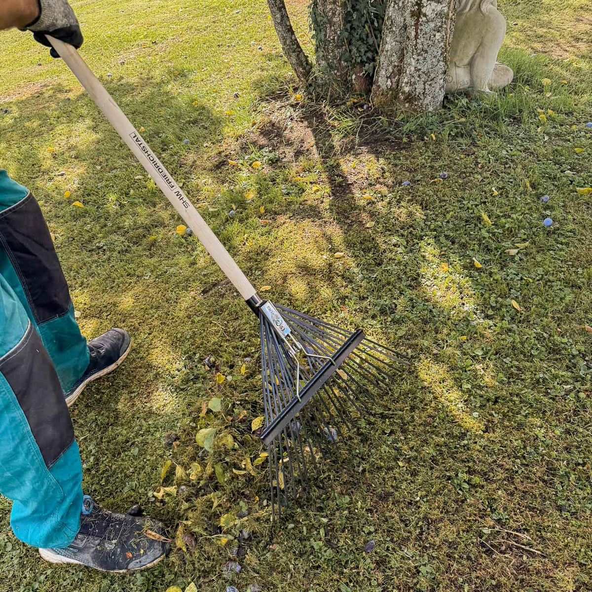 Gärtner beim Zusammenrechen von Laub und Gartenabfällen auf einer Rasenfläche mit dem verstellbaren SHW Laubbesen Profi.